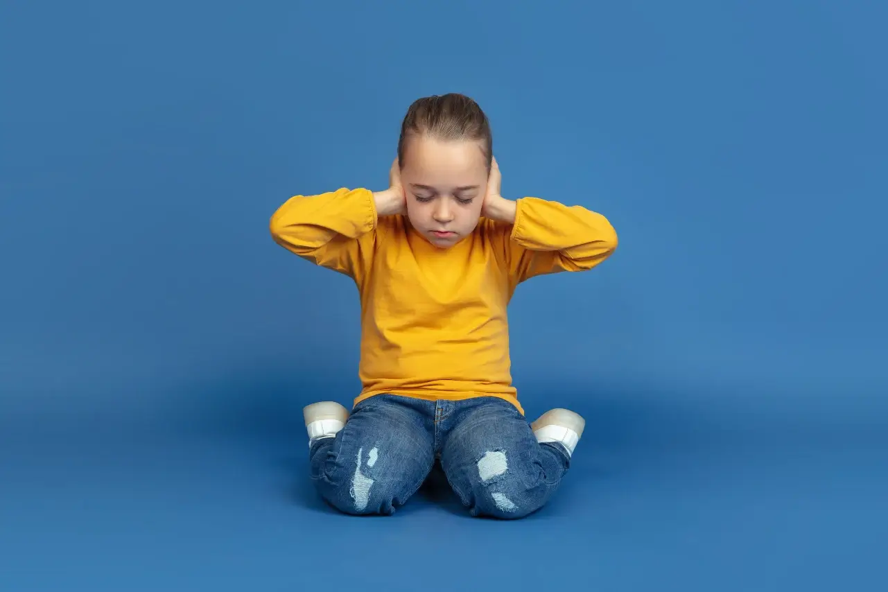 Dziewczynka w wieku przedszkolnym zatykająca uszy rękoma, z zamkniętymi oczami. Autyzm dziecięcy. Spektrum Autyzmu