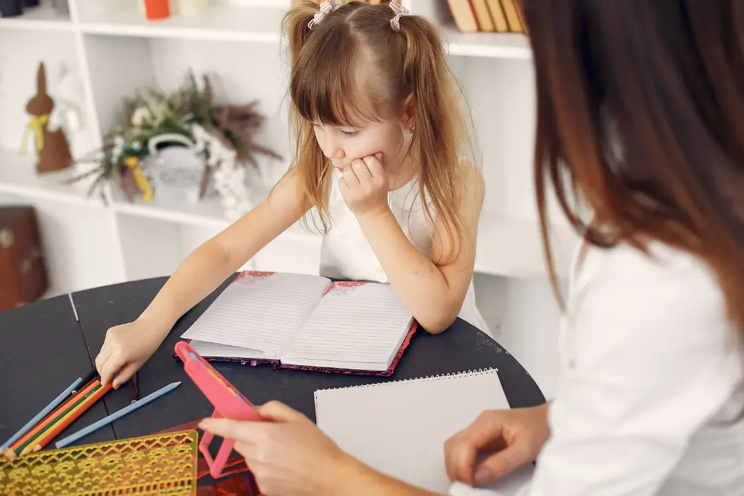 Dziewczynka pochylona nad kartą papieru i Pani Psycholog dziecięca z otwartym notatnikiem.
